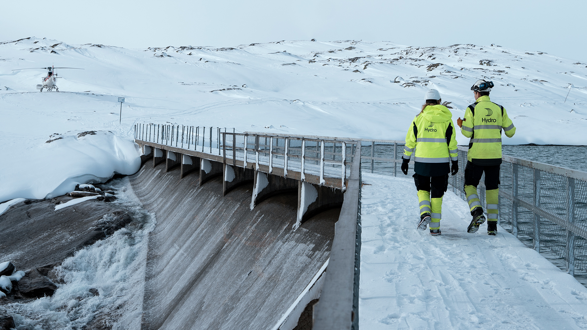 a couple of people walking on a bridge over a snowy mountain