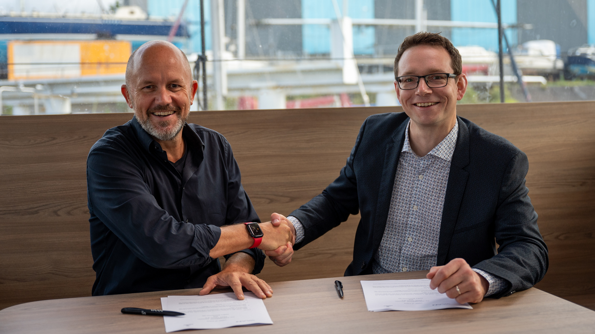 a couple of men sitting at a table with papers and pens