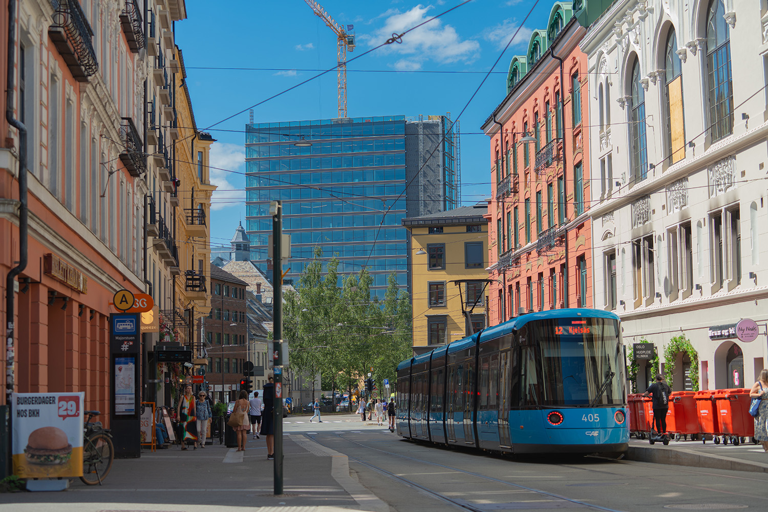 a blue train on a street with buildings and people walking