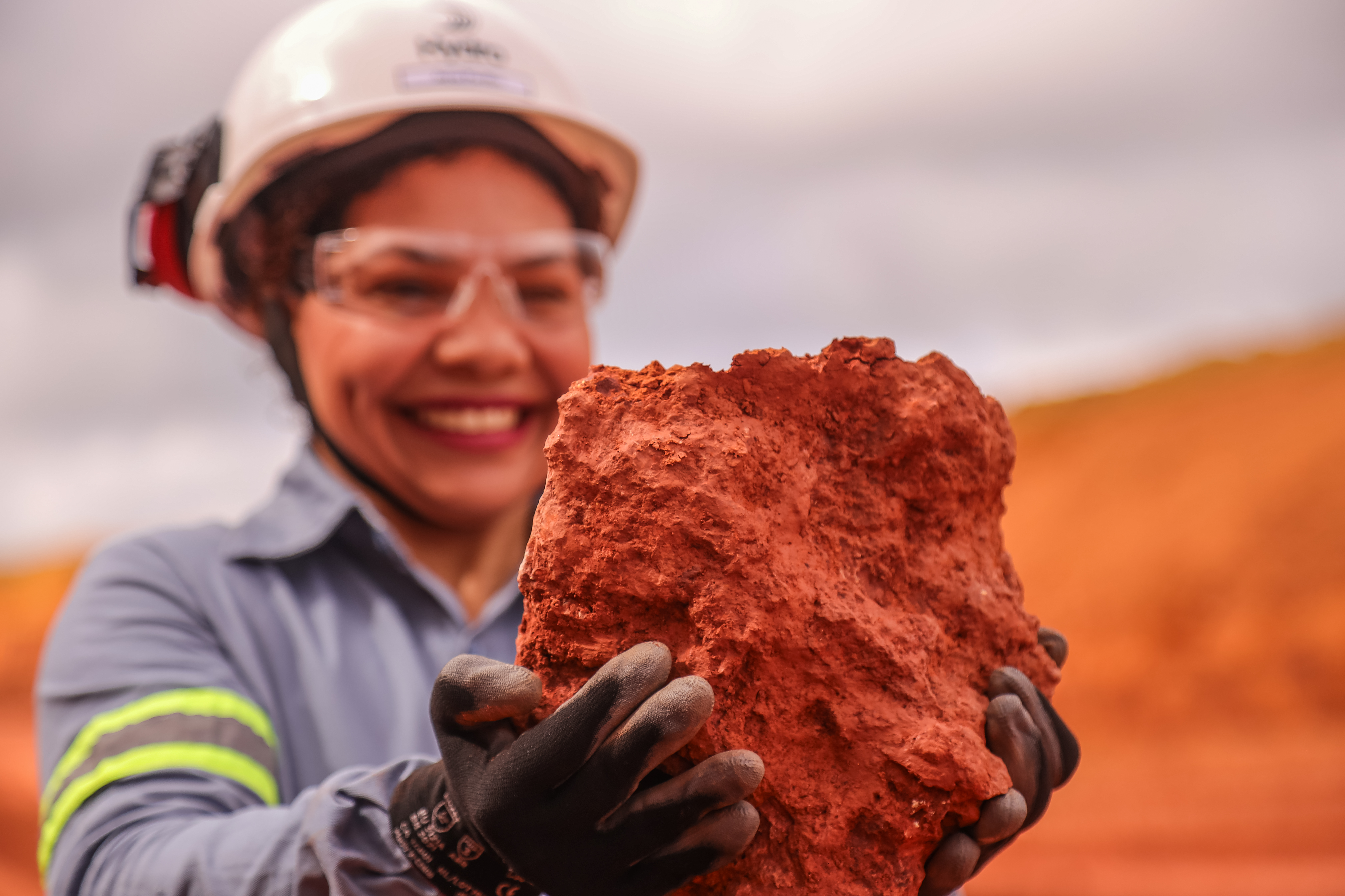 a woman wearing hard hat and gloves holding a large red rock